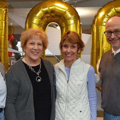 Annie Nell Wadley, Kathy Gosser, Denise Cumberland, and Troy Price stand in front of gold balloons with the number 100 in Frazier Hall