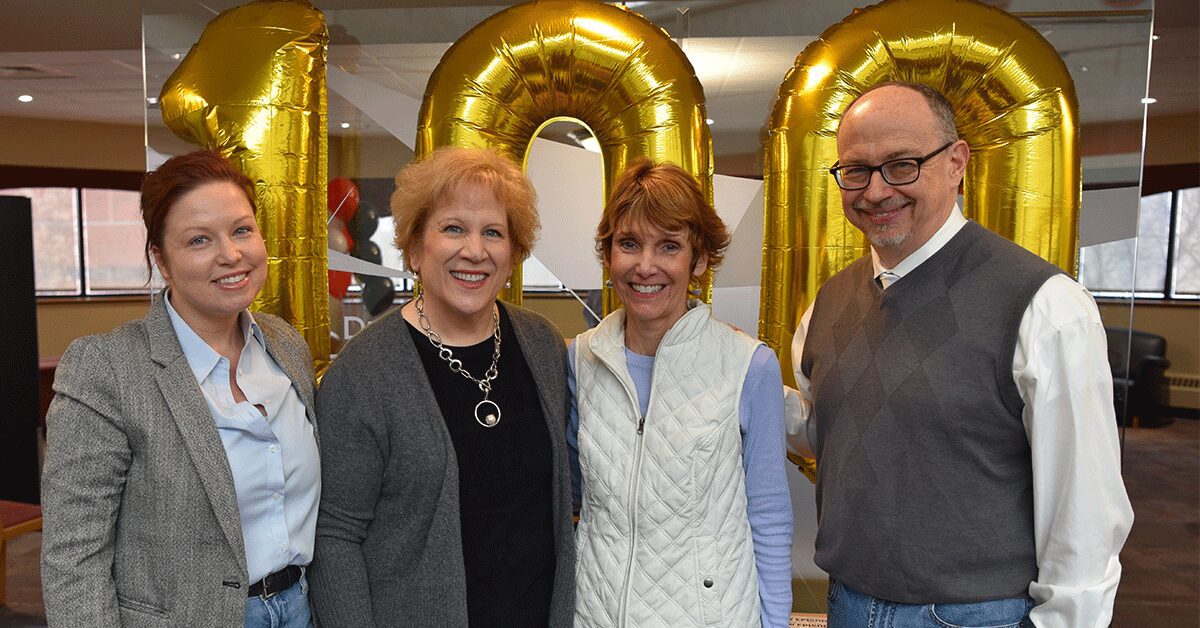 Annie Nell Wadley, Kathy Gosser, Denise Cumberland, and Troy Price stand in front of gold balloons with the number 100 in Frazier Hall