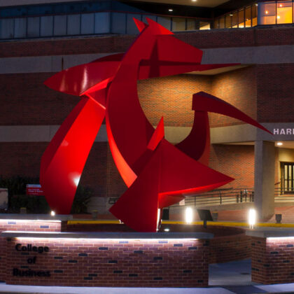 The front of Frazier hall at night with sculpture in foreground.