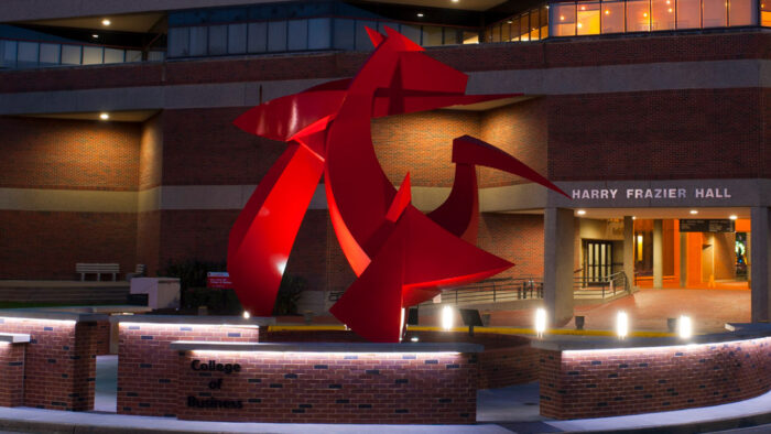 The front of Frazier hall at night with sculpture in foreground.