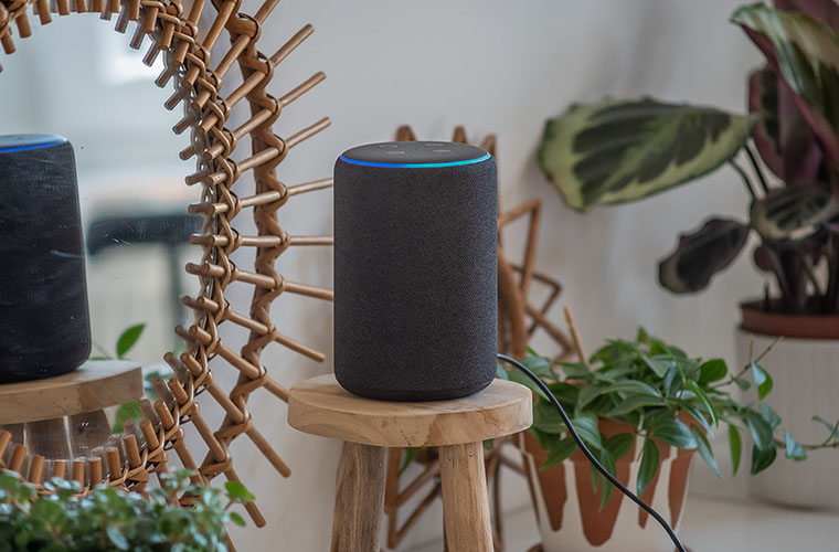 Amazon Alexa Echo Plus en una mesa de madera con plantas verdes en el fondo
