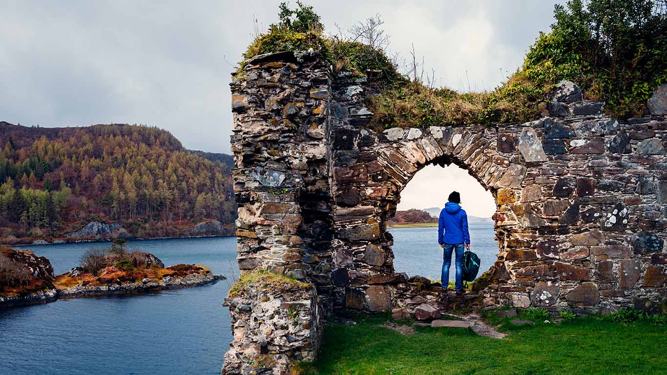 Женщина турист на руинах замка Strome на берегах озера Лох Каррон в регионе Wester Ross Шотландии.