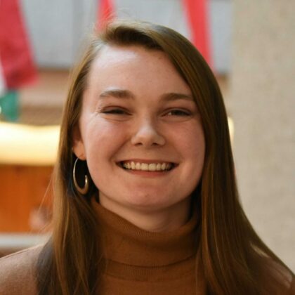 UofL student Tessa Chilton headshot. She's wearing a brown turtleneck and standing in the CoB atrium.