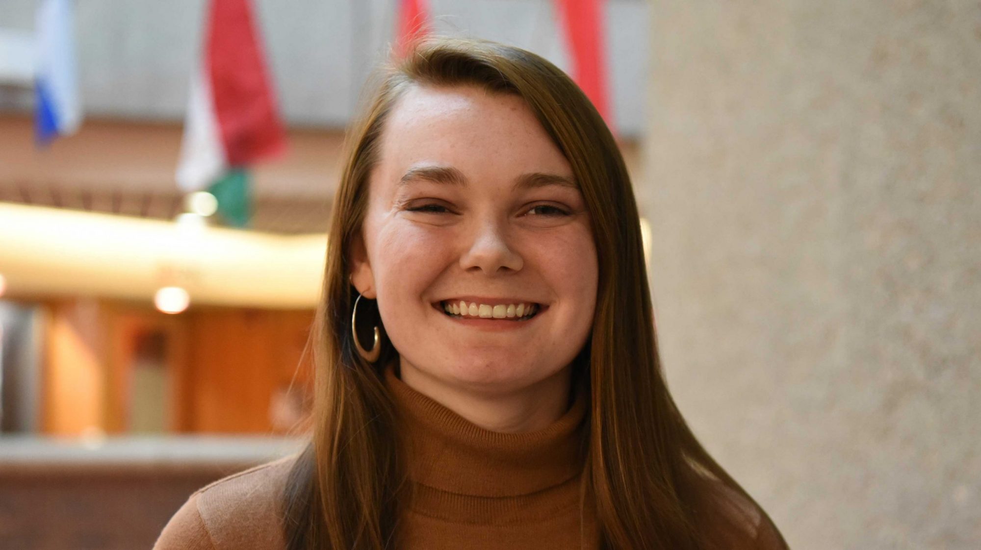 UofL student Tessa Chilton headshot. She's wearing a brown turtleneck and standing in the CoB atrium.