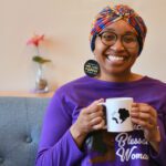 Arielle Clark sits on a gray couch holding a mug with the logo of her cafe, Sis Got Tea.