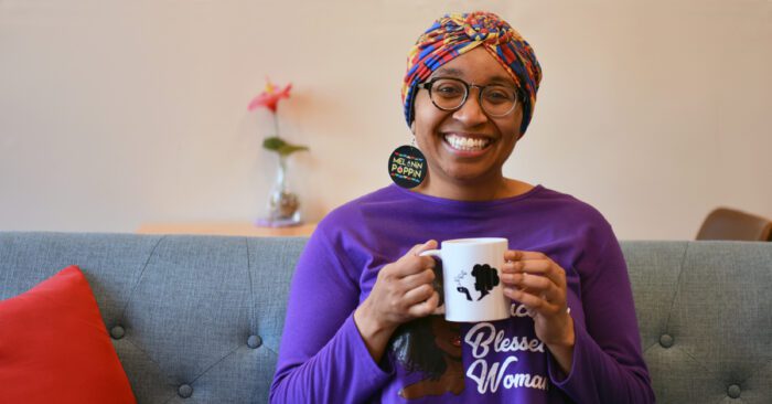 Arielle Clark sits on a gray couch holding a mug with the logo of her cafe, Sis Got Tea.