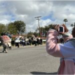 3-year-old Jorgie taking photos of parade in the street with pink camera