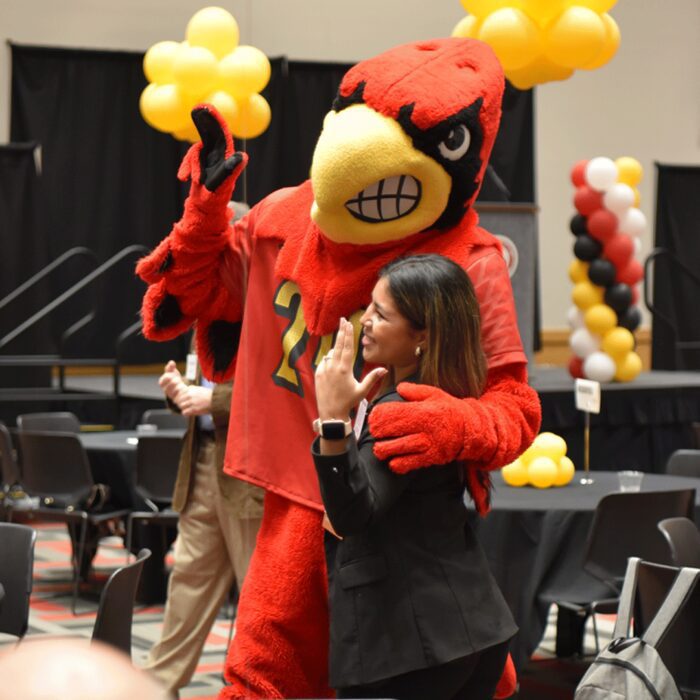 Justyne Aranda and Louie the Cardinal mascot pose with their Ls up for a photo