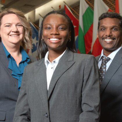 Sakthiraj Kandasamy, Susan Miracle and Hope Odubena stand in front of international flags in Frazier Hall on the UofL campus