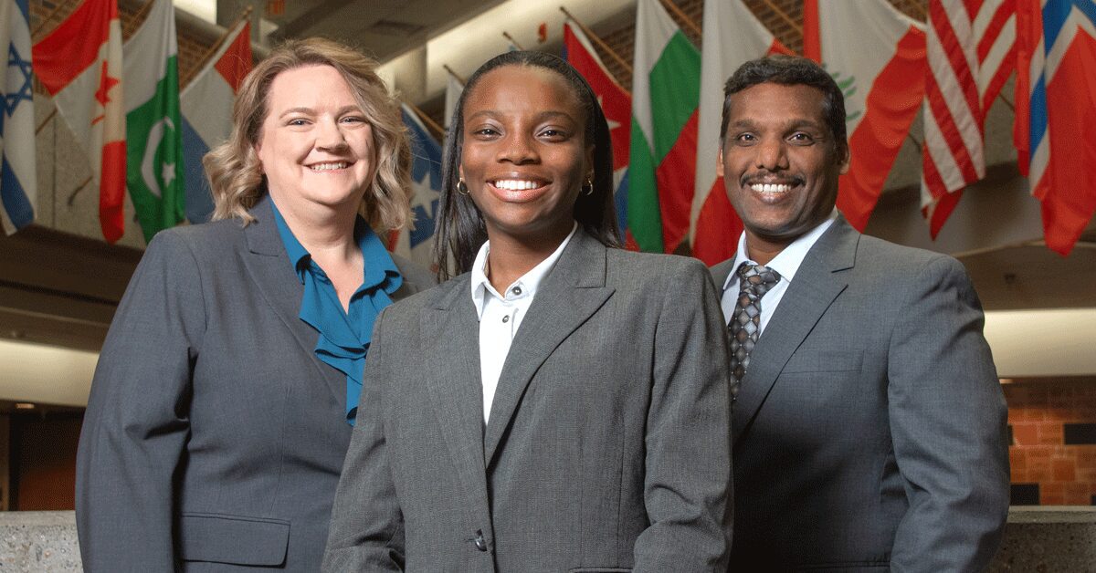 Sakthiraj Kandasamy, Susan Miracle and Hope Odubena stand in front of international flags in Frazier Hall on the UofL campus