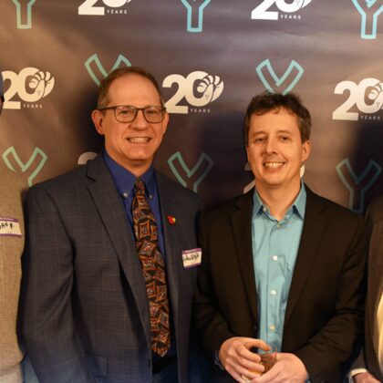 Dan Murphy, Andrew Wright, David Galownia, and Robert Barker stand in front of the Slingshot 20th anniversary backdrop