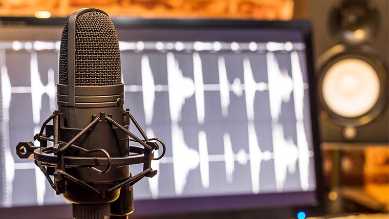 Nahaufnahme eines Podcast-Mikrofons mit Adobe Audition Software auf dem Computerbildschirm im Hintergrund.