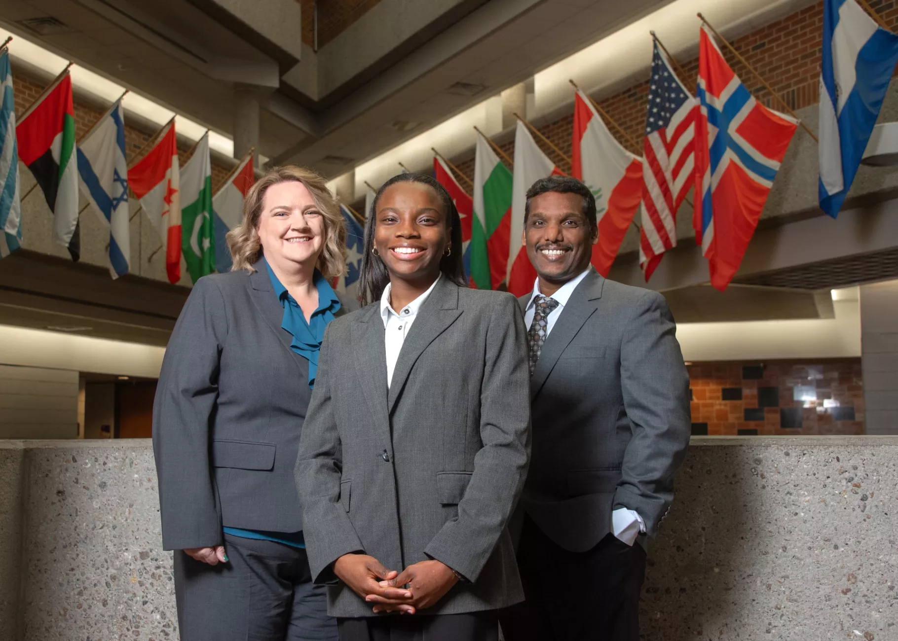 Sakthiraj Kandasamy, Susan Miracle and Hope Odubena in front of flags in College of Business atrium.