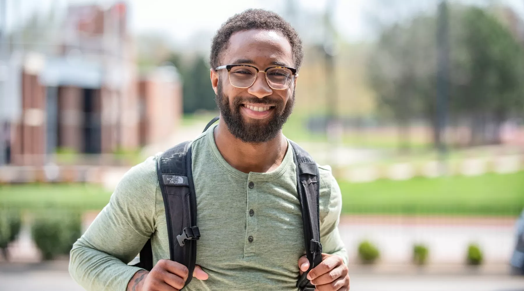 Undergrad student holding backpack and smiling on campus