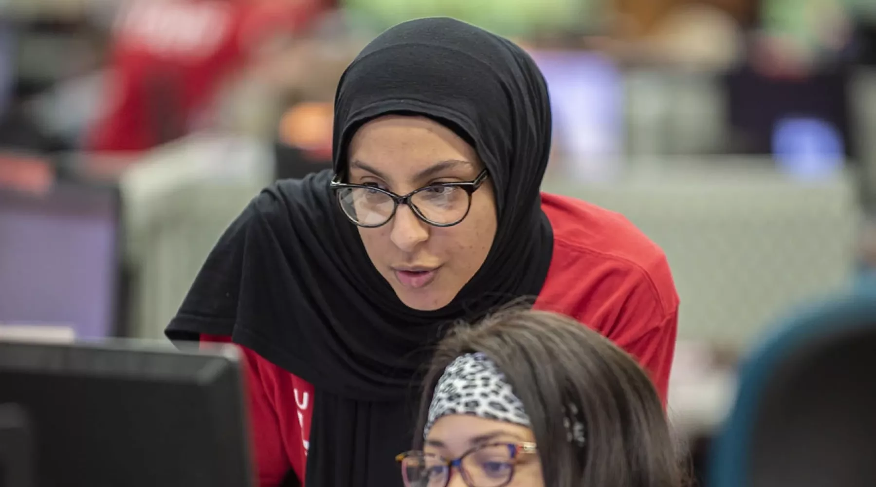 College of Business student overlooks another student's shoulder at a computer screen in the computer lab.