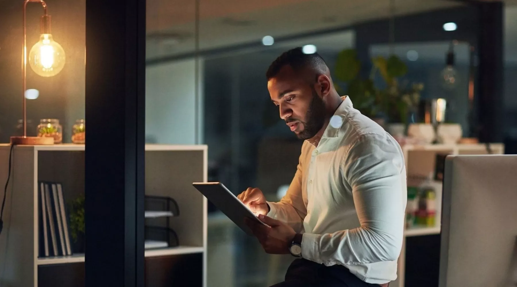 Man in business attire using a tablet computer in an office at night.