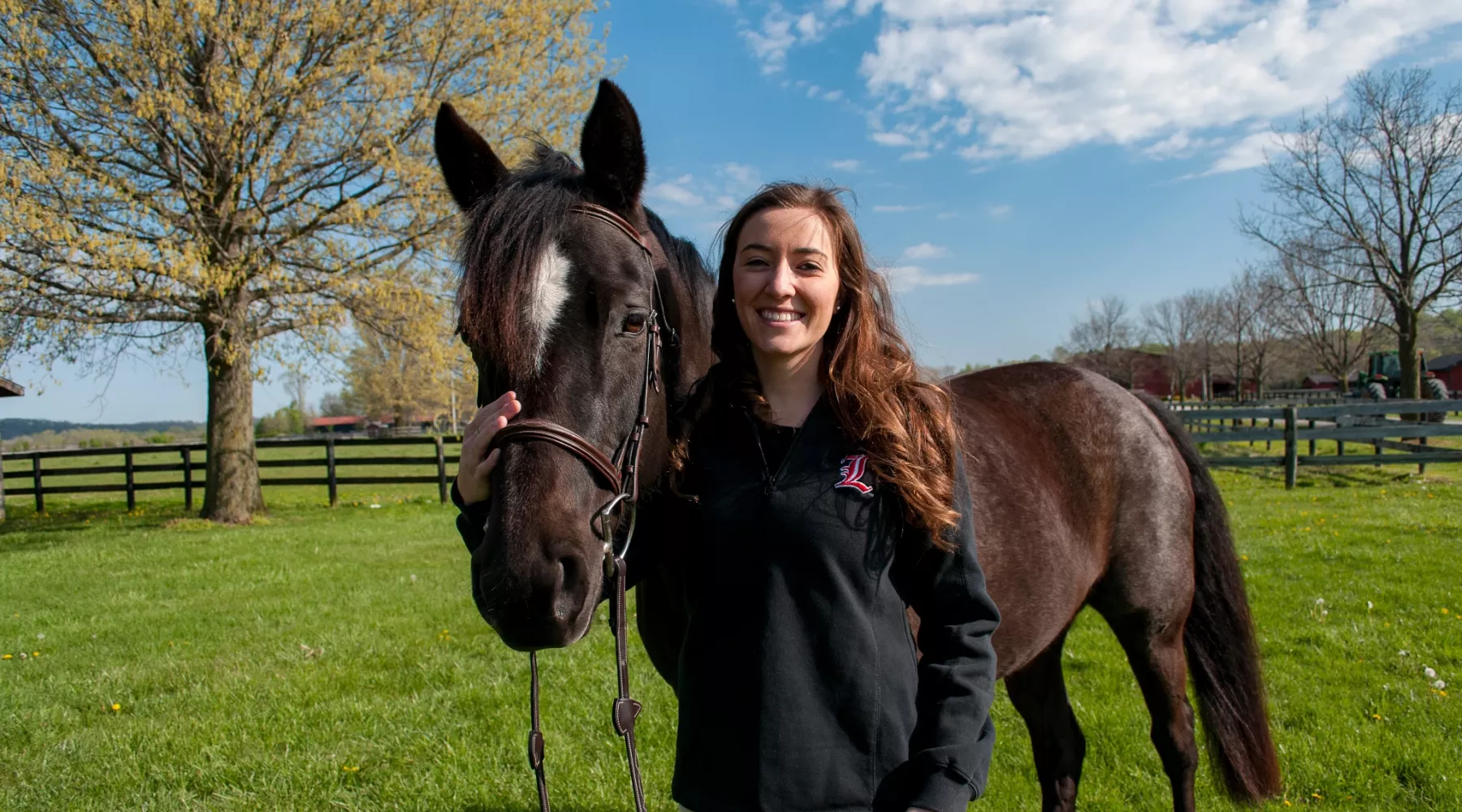 UofL College of Business student poses next to a brown horse, petting its face and holding its reigns.