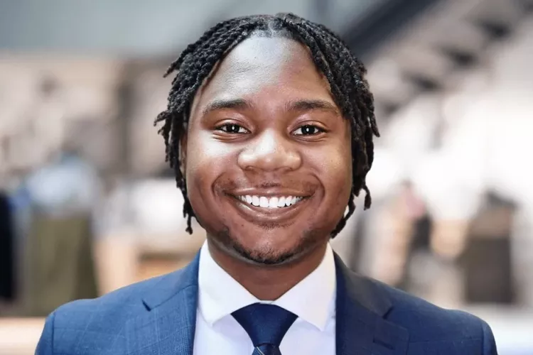 Golden Mashindi in blue suit and tie in front of blurred background.