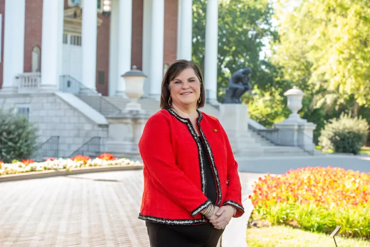 Woman in Cardinal red blazer standing in front of building with columns and bronze statue of The Thinker on UofL's Belknap…