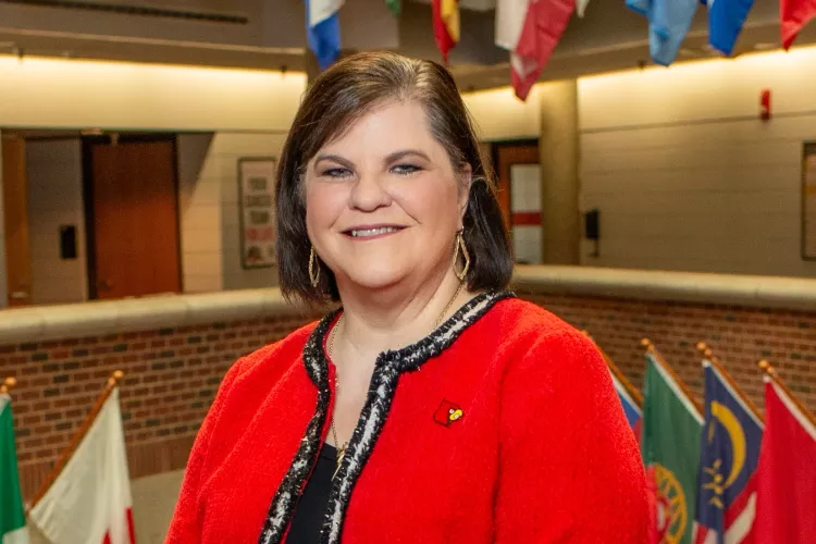 Woman in Cardinal red blazer posed for photo with country flags hanging in the background.