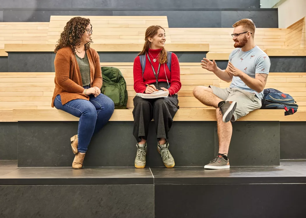 Alison Williams sitting on the wooden benches within the entrance of the Belknap Academic Building