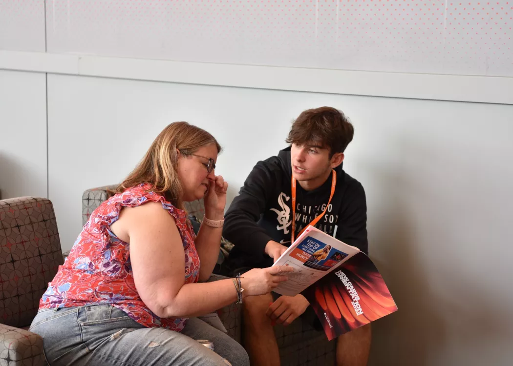 Student and parent reading the orientation magazine at New Card Orientation University of Louisville College of Business.