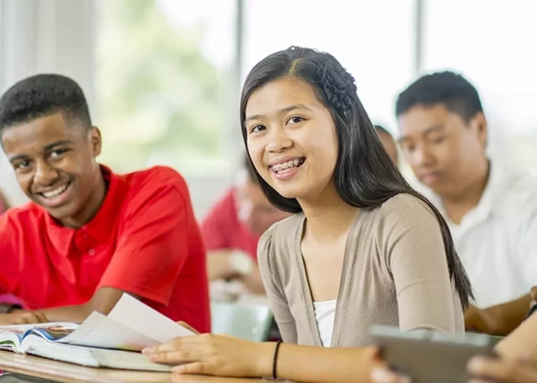 A smiling young grade school female and male student read a textbook together