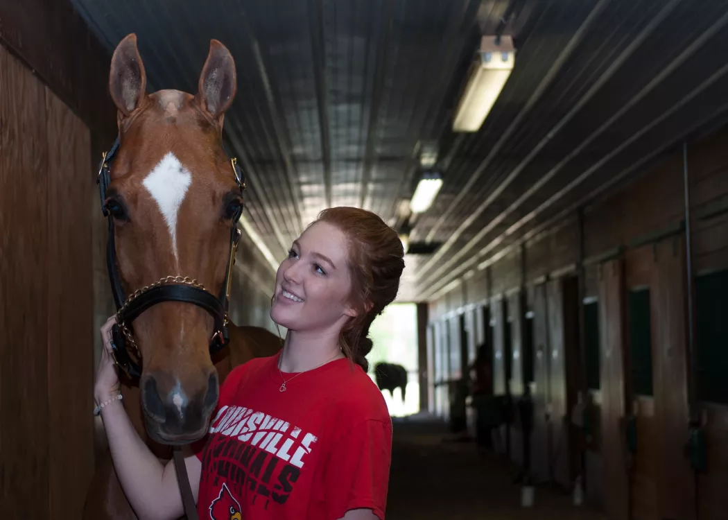 UofL College of Business student stands next to a light brown horse
