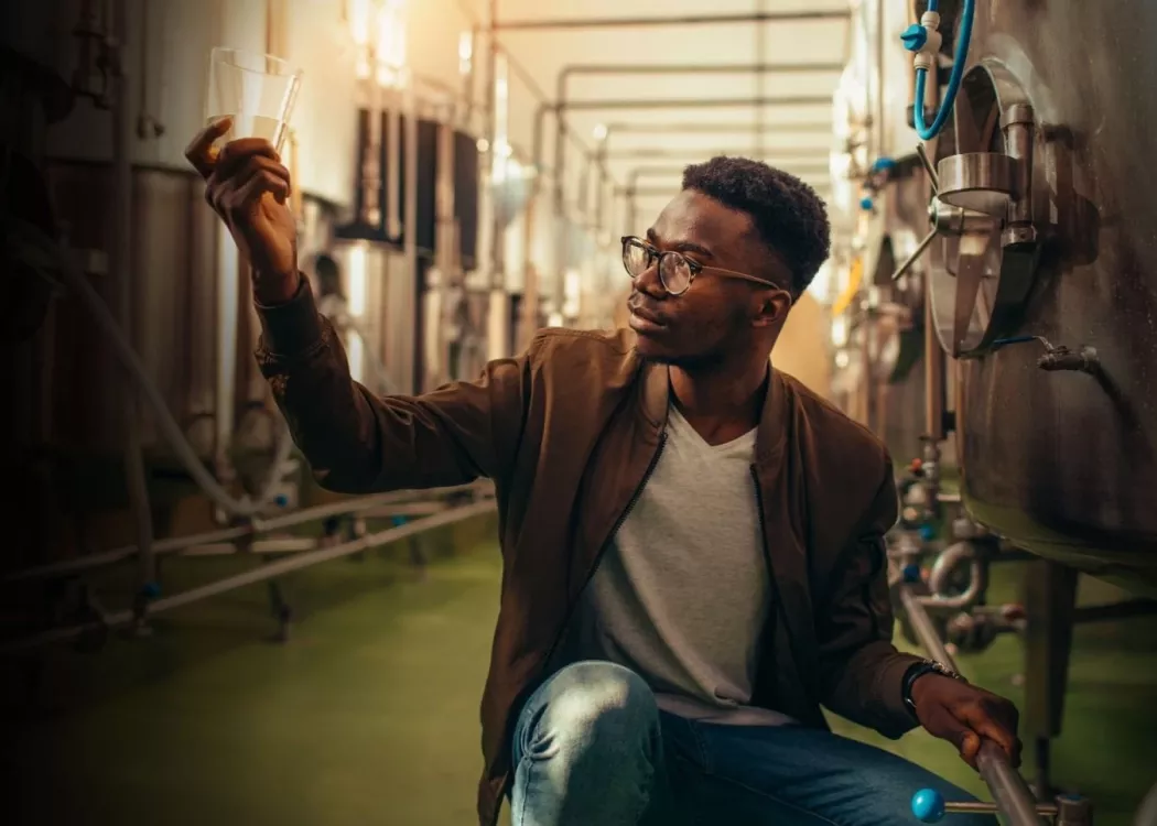 Man analyzes alcohol next to distillery equipment