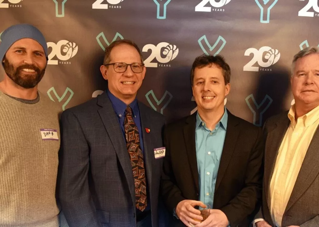 Four men posing in front of a banner.