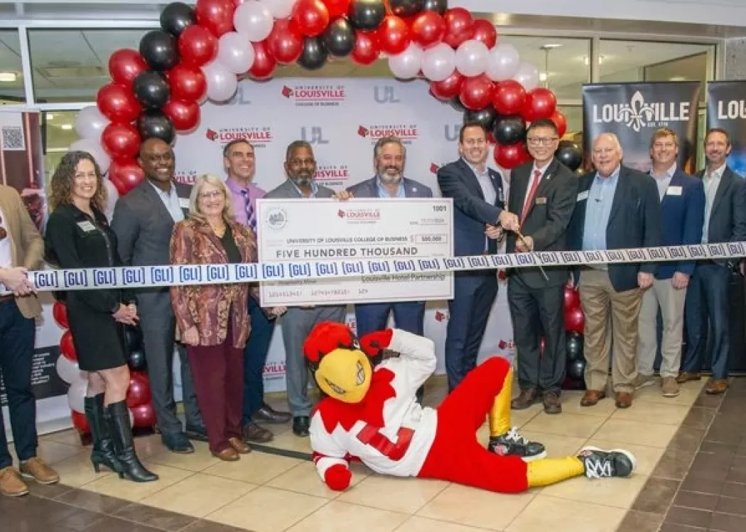 Louie the Cardinal posing on the floor in front of a crowd holding a large check.