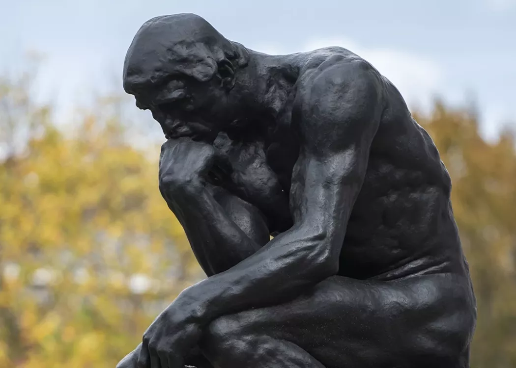 The thinker statue with blurred trees in the background