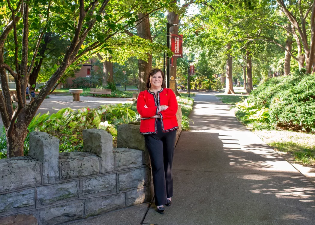 Dean Amy Henley in red blazer standing with arms crossed in Belknap Quad.