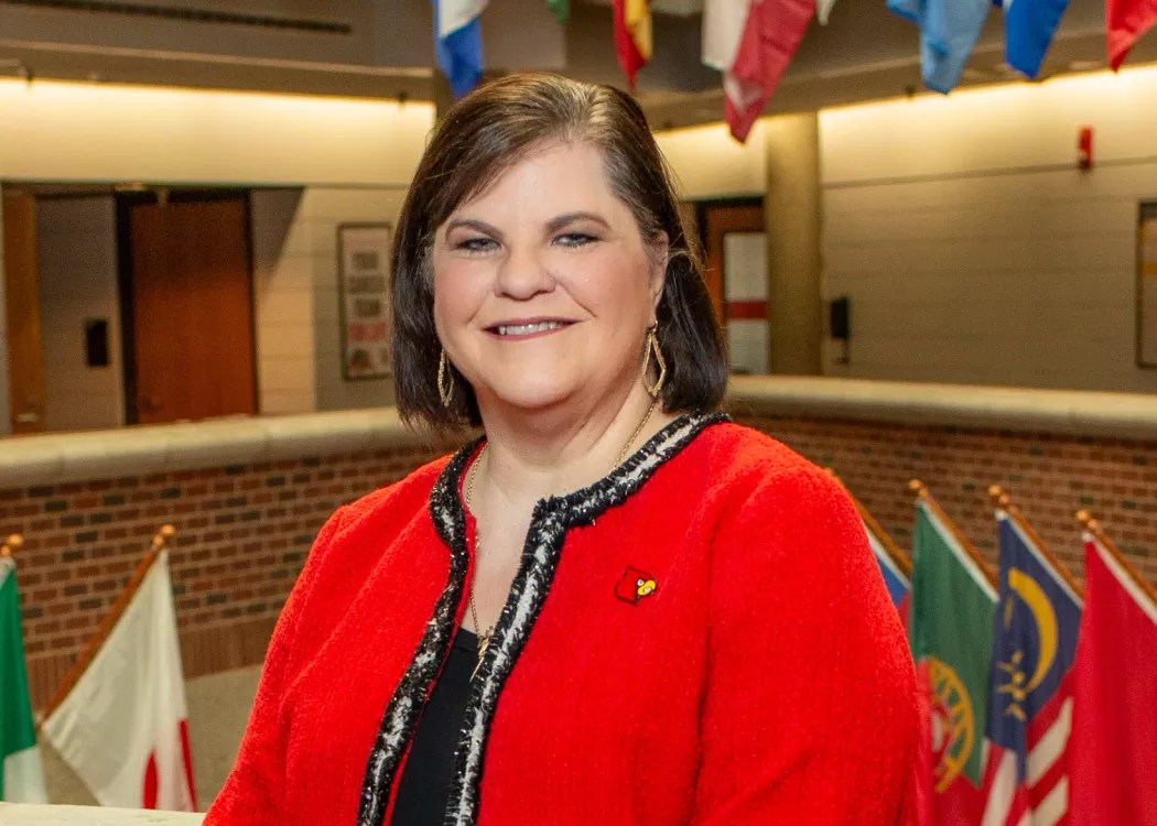Woman in Cardinal red blazer posed for photo with country flags hanging in the background.