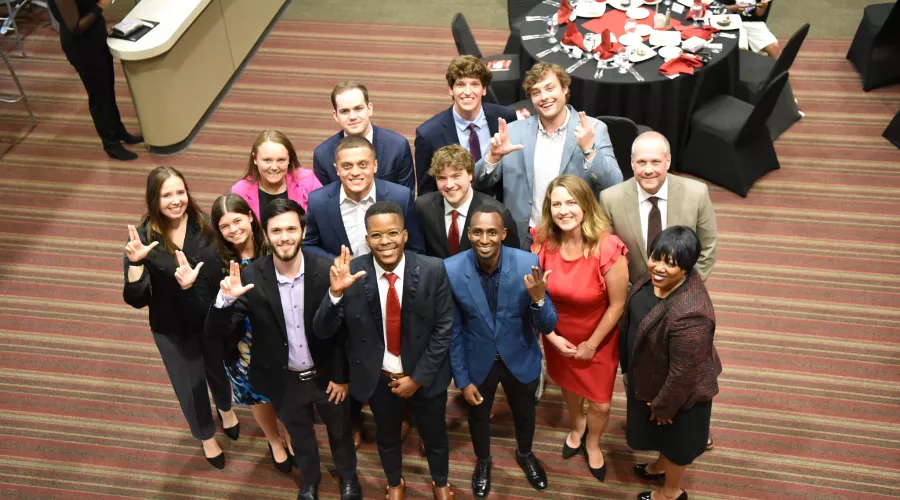 Participates of the MSBA and MSAA program staring up at camera holding up the "L" hand symbol at the MSBA and MSAA Grad Dinner