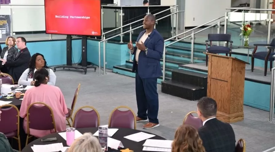 A suited man delivering a presentation in front of a crowd.
