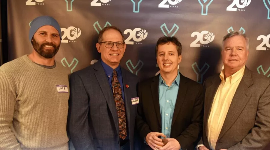 Four men posing in front of a banner.