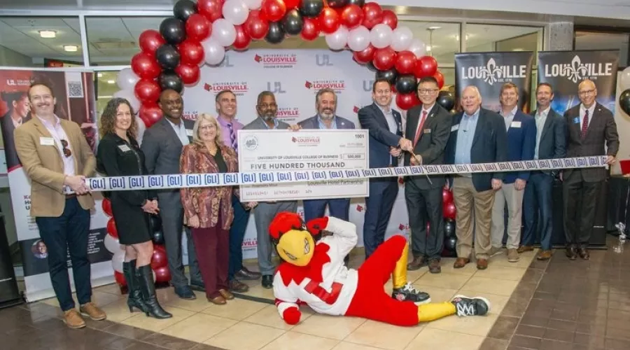 Louie the Cardinal posing on the floor in front of a crowd holding a large check.