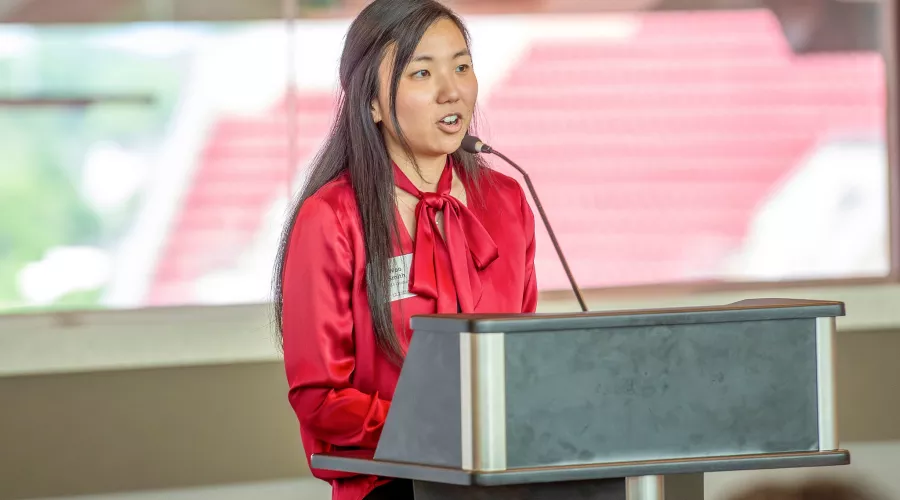 Fall22 PMBA President, Woo Smith,  gives speech at podium  to the graduating class at PNC Club. A window is in the…
