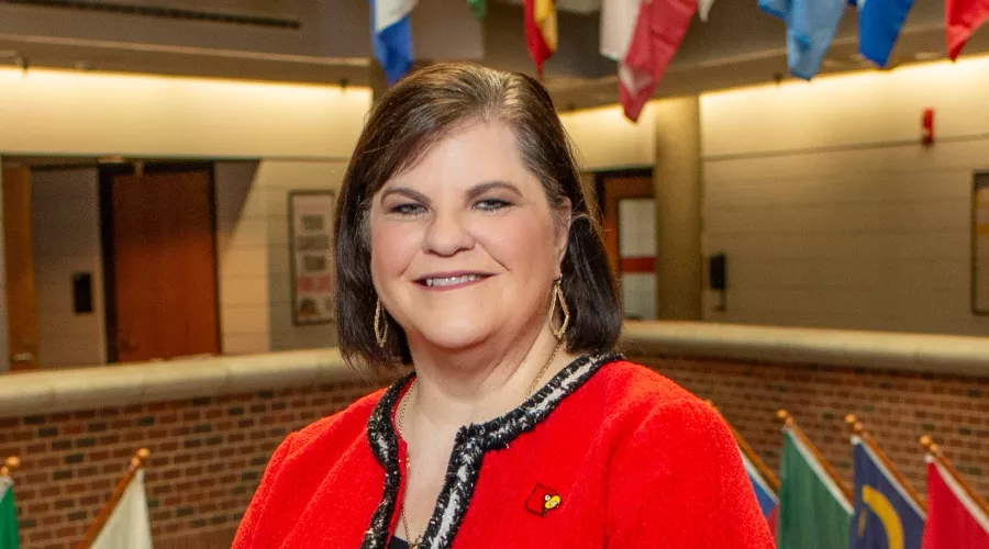 Woman in Cardinal red blazer posed for photo with country flags hanging in the background.