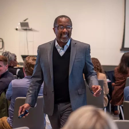 UofL College of Business Professor, Nat Irvin, in the center of a seated crowd smiling, walking and talking at a summit event
