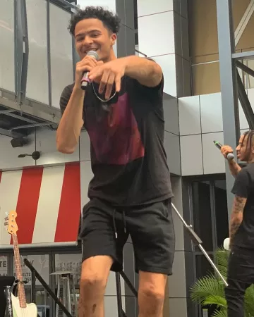 A man pointing towards the camera as he speaks into a microphone.