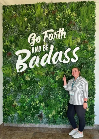 A woman pointing to a large banner reading "Go Forth and be Badass".